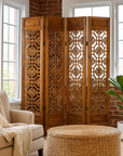 Beige four-panel screen with geometric fretwork motifs next to a beige sofa and plant in a bright, cozy room.