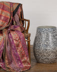 Pink and gold patterned fabric draped over a chair next to a large ceramic planter vase on wooden floor.