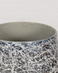 Black, gray, and white ceramic planter vase with abstract pattern on wooden floor against a white wall.