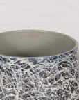 Black, gray, and white ceramic planter vase with abstract pattern on wooden floor against a white wall.