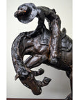 Bronze Frederic Remington "Rattlesnake" tabletop statue of cowboy on bucking horse, Western art style, on table.