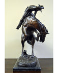 Bronze Frederic Remington "Rattlesnake" tabletop statue of cowboy on bucking horse, Western art style, on table.