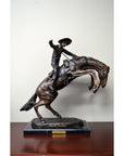 Bronze "Bronco Buster" Frederic Remington statue on marble base, displayed on wooden shelf.