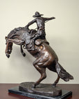 Bronze Remington statue of cowboy riding rearing horse, close-up view, displayed on a tabletop.