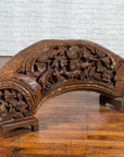 Brown wood arch sculpture with hand-carved animal and floral motifs on a dark antique chest.