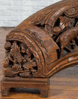 Brown wood arch sculpture with hand-carved animal and floral motifs on a dark antique chest.