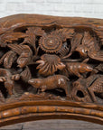 Brown wood arch sculpture with hand-carved animal and floral motifs on a dark antique chest.