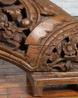 Brown wood arch sculpture with hand-carved animal and floral motifs on a dark antique chest.