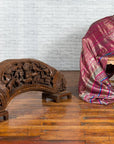 Brown wood arch sculpture with hand-carved animal and floral motifs on a dark antique chest.