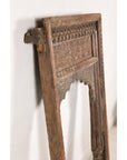 Brown wooden hand-carved Indian architectural frame with arched opening leaning against a white textured wall.