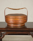 Brown woven rattan Chinese basket with painted cover and handle on a wood table.