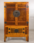 Antique Chinese elm and burl cabinet with brass hardware beside a pedestal with dried flowers.
