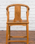 Brown elmwood Chinese Qing Dynasty chair with carved medallion, on wood floor against white brick wall.