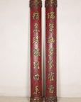 Pair of tall red and gilt Chinese calligraphy panels displayed against a pale wall