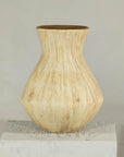 Beige textured ceramic vase with drip glaze and flared neck on white wooden pedestal.
