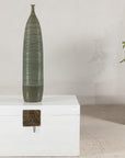 Green-glazed ceramic vase with a ribbed body on a white wooden chest.
