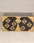 Black lacquered vintage Chinese chest with gold geometric decoration and central latch on a plain floor.