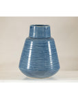 Blue-glazed ceramic vase with tapering form on a white surface, neutral background, close-up.