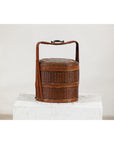 Brown vintage woven box with double handles on white textured pedestal, plain background, close-up.