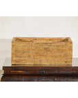 Brown rattan long rectangular storage box with lid on a dark carved wooden table against a plain background.