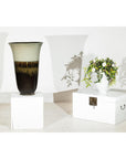 Green-grey and brown ceramic planter with drip glaze on white boxes against plain background, close-up.