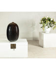 Deep brown and black glazed ceramic vase with honeycomb texture on white chest, white vase in background.