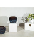 Close-up of two vintage blue and aqua glazed ceramic planters next to a white vase with flowers, shadows on wall.