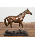 Bronze horse tabletop sculpture on black marble base, displayed on wood floor with white brick wall background.