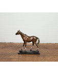 Bronze horse tabletop sculpture with black marble base on wood floor against white brick wall.