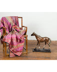 Wooden chair with pink patterned fabric next to contemporary bronze horse tabletop sculpture on wooden floor.