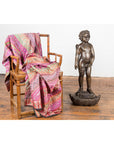 Patterned pink shawl draped on a chair next to a bronze winged cherub statue on a wooden floor.