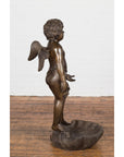 Dark patina bronze winged cherub statue on a shell, profile view, against a white brick wall background.