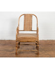 Brown hand-woven rattan armchair with rounded back on wooden floor by a white brick wall, country vintage style.