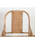 Natural rattan armchair with rounded back, hand-woven in Burmese vintage style, set against a white brick wall.