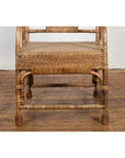 Brown rattan armchair with rounded back, hand-woven vintage style, on wooden floor against white brick wall.