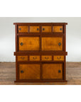 Two-tone wood Japanese Taishō Mizuya Dansu kitchen cabinet with sliding doors on wooden floor by white wall.