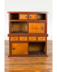 Two-toned wood Japanese Taishō Mizuya Dansu kitchen cabinet with sliding doors, on wooden floor against white wall.