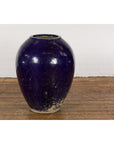 Cobalt blue glazed ceramic water vessel with tapering lines on wooden floor against a white brick wall.