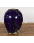 Cobalt blue glazed ceramic water vessel with tapering lines on wooden floor against white brick wall.