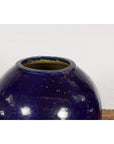 Cobalt blue glazed ceramic Thai water vessel with tapering lines, displayed against a white brick wall.