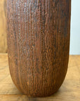 Close-up of brown and copper ceramic vase with vertical grooves on wooden surface.