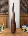 Brown and copper textured ceramic vase on table between two figurines, near books and wood panels.
