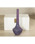 Purple ceramic vase with slender neck, artisan style, in front of a white chest on a beige floor.