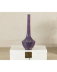 Purple ceramic vase with slender neck on white chest with metal clasp, close-up.