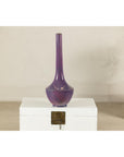 Purple glazed ceramic vase with slender neck on a white chest, light background, close-up.