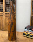 Sand brown and orange ceramic vase with black crackle design on a wooden table next to books and wood panels.