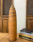 Orange ceramic vase with black swirl on wooden table next to stacked antique and design books.