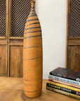 Orange ceramic vase with black swirl next to books on a wood table with carved wood backdrop.