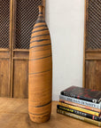 Orange and black ceramic vase with swirl design on wooden table beside books, wood panel background.