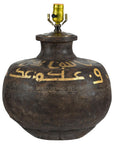 Close-up of a vintage brown metal jug lamp with gold Arabic script and brass socket, patina visible.